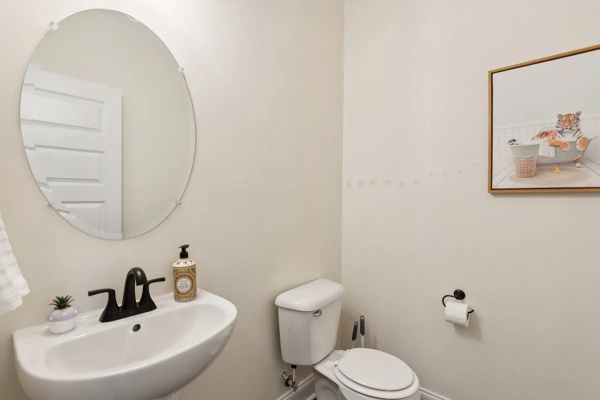 A stylish powder room featuring an oval mirror, modern sink and faucet, tasteful framed artwork, and a toilet. The design is compact, emphasizing efficiency and aesthetics in a smaller space.