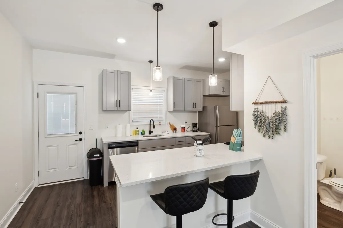 This image showcases a modern kitchen with a central island, sleek appliances, and stylish pendant lighting. The space is arranged for both meal preparation and social interaction, with visible cookware and utensils that reinforce the idea of a fully equipped, ready-to-use kitchen.