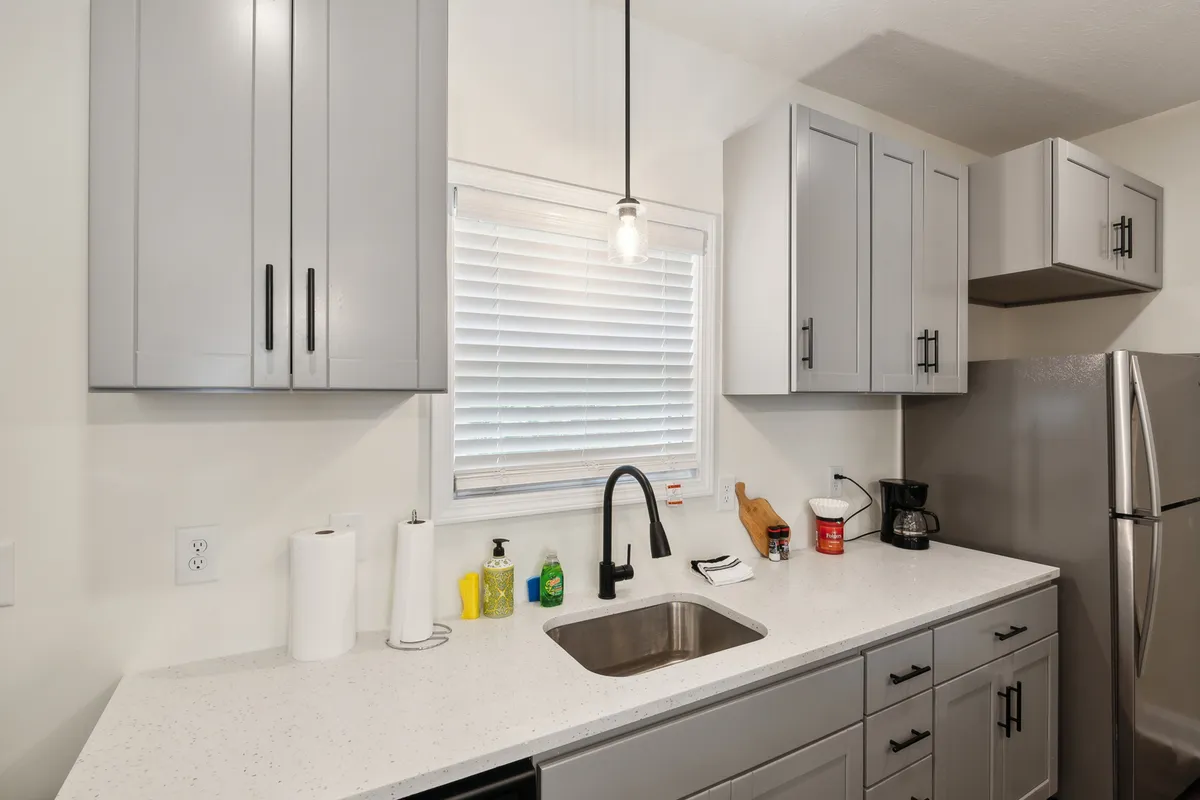 Focusing on the kitchen sink, countertop, classic cabinetry, and a bright window, this image showcases the practical side of meal preparation. Baking tools and cozy lighting suggest everyday usability and homeliness, rounding out the overall kitchen story.