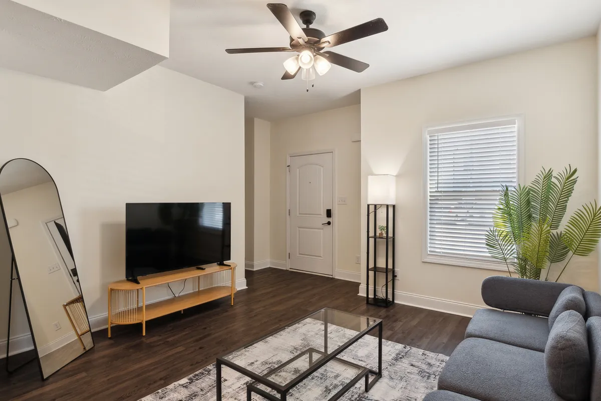The image showcases a stylish living room featuring a plush sofa, a modern coffee table, a sleek television, a floor lamp casting a warm glow, and a vibrant plant that adds a touch of freshness. The arrangement creates a cozy, inviting space perfect for relaxation or gathering with friends.