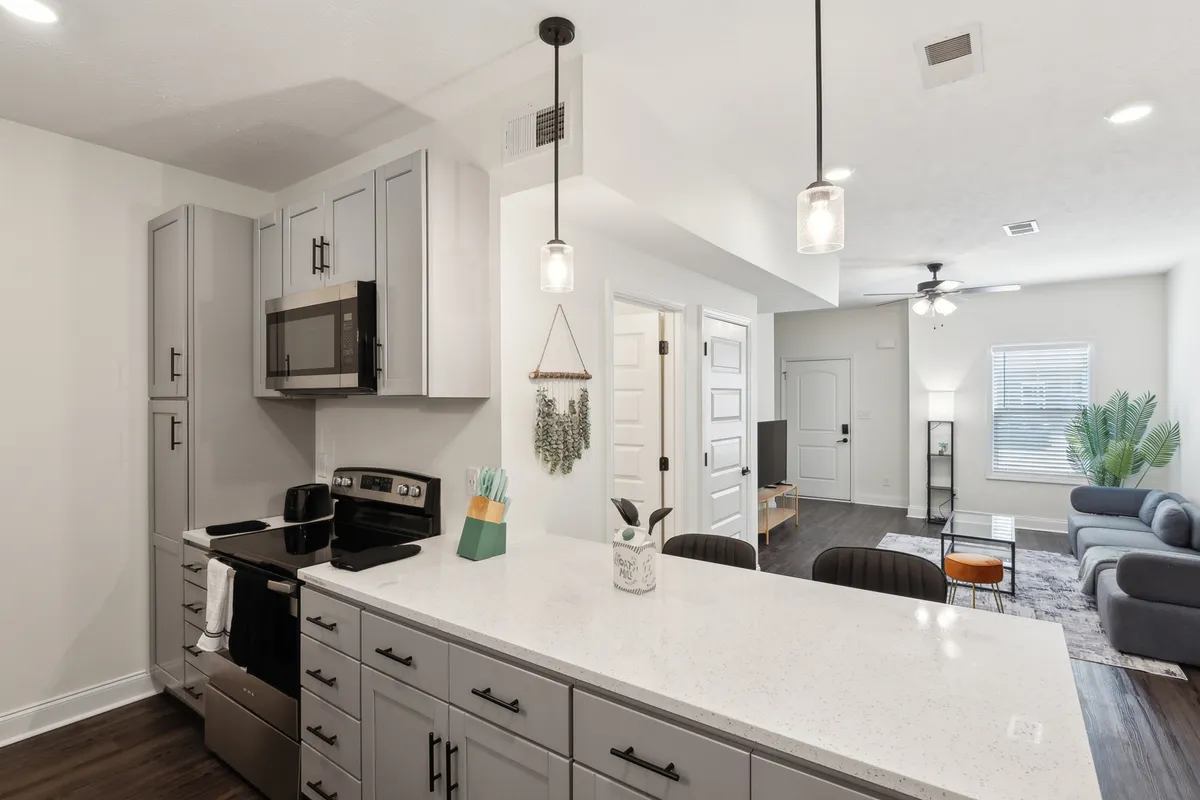 This image offers a wide-angle view of the kitchen, highlighting a contemporary island with modern appliances and a glimpse into the connected living area. The open-plan design emphasizes versatility and the ability to entertain or relax, echoing the section’s focus.