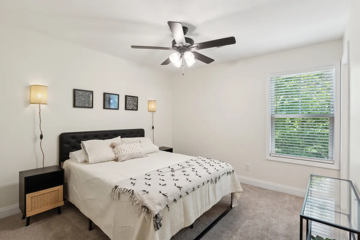 A cozy bedroom with a well-dressed bed, nightstands on either side, and a large window letting in gentle morning light. The space feels inviting and perfectly suited for restful nights or enjoying a good book.